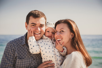 Fototapeta premium Close up of young happy loving family with small kid in the middle, having fun at beach together near the ocean, happy lifestyle family concept