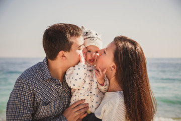 Close up of young happy loving family with small kid in the middle, kissing each other near the ocean, happy lifestyle family concept