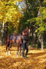 Equestrian girl walks bay arabian horse in autumn woods