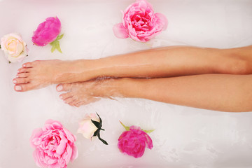 Obraz na płótnie Canvas Woman with beautiful legs taking a bath with flowers.