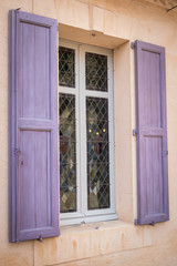 Window with purple shutters in an old facade in Mediterranean style.