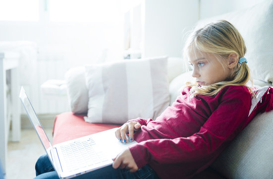 Happy  little girl lying on the sofa with laptop in the living room at home.