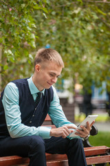 A young guy is sitting on a park bench with a phone in his hands