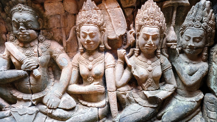 3 apsara ladies and giant bas relief on pink grey sandstone at Angkor Thom, Siem Reap, Cambodia