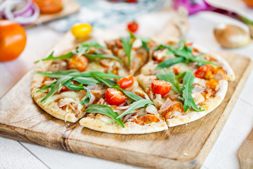 hot fresh homemade traditional italian pizza with cheese, tomatoes and rocked salad on wooden cooking table. wallpaper for pizzeria and food concept