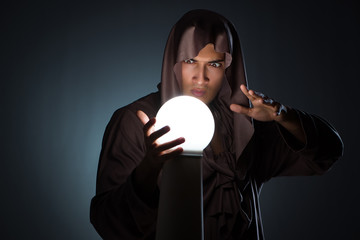 Young wizard with crystal ball in dark room