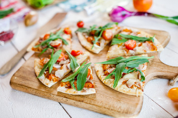 hot fresh homemade traditional italian pizza with cheese, tomatoes and rocked salad on wooden cooking table. wallpaper for pizzeria and food concept
