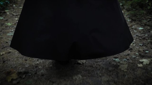 A woman in a long black cloak with a hood is walking along the park, the lady is walking with her back to us, we do not see her face