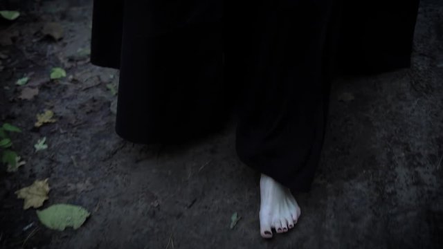 close up shot of the pale feet of a woman who walks barefoot along the gray park road, a woman dressed in a long dress