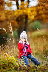 Cute little girl having fun on beautiful autumn day. Happy child playing in autumn park. Kid gathering yellow fall foliage.