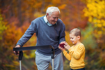 Young grandson showing something on phone in the park disabled senior grandfather