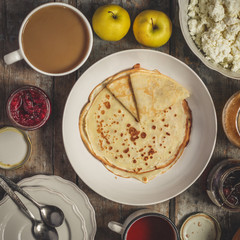 Pancakes and serving on a wooden table (honey, jam, tea, coffee, cappuccino, cocoa, cottage cheese, apples, pumpkin, etc.)