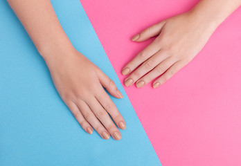 Closeup of hands of a young woman with manicure on nails against pink background