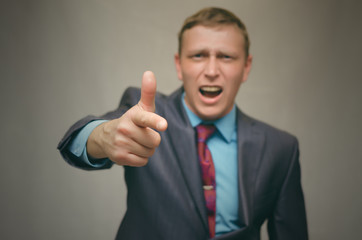 Angry business man in a suit swears and screams at someone and pointing at him with his index finger. Strict angry boss. Man proves his rights.