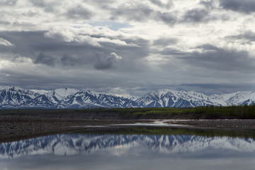 Spring mountains with remnants of snow and the reflection in the river. The River Indigirka....