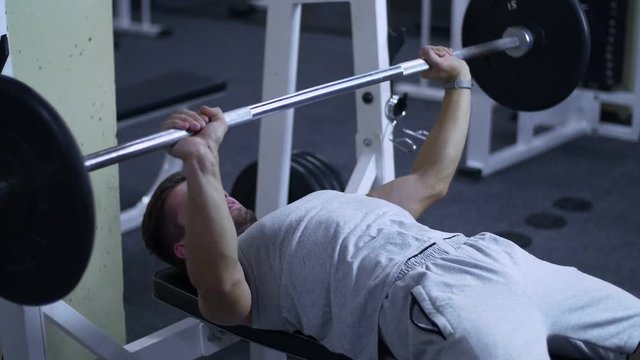 Strong male bodybuilder doing bench press exercise with heavy barbell in gym