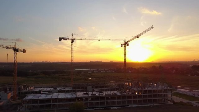 Building cranes at construction site against sunset sky. Aerial shot