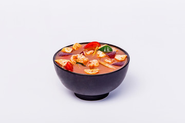 Spicy Thai soup Tom Yam with seafoodon in a black bowl on a white background