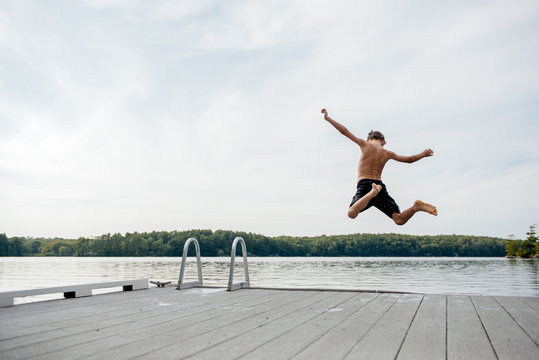 Child jumps off a dock into a lake on a summer evening