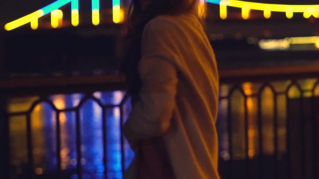 Slow motion. a young blonde girl with long curly hair dances in the night gown on the background of glowing fanfare. bright night illumination and a luminous bridge. The professional dancer moves