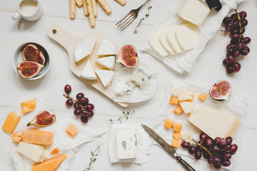 Various types of cheese with fruits and snacks on the wooden white table. Top view