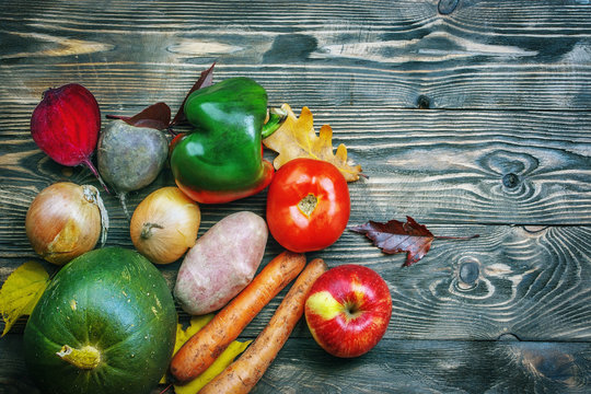 Creative image of vegetables on a .wooden background. Pumpkin, potatoes, tomato, onions, carrots, peppers, apple.
