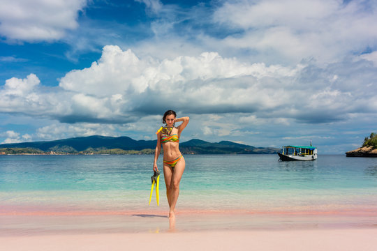 Beautiful young woman smiling while holding snorkeling equipment at Pink Beach during summer vacation in Komodo Island, Indonesia