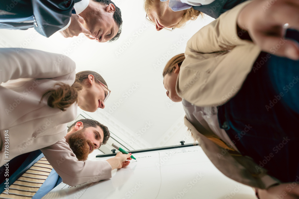 Wall mural Low-angle view of the members of an international team working together for finding solutions during brainstorming session in the office