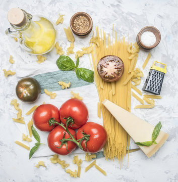 concept of cooking Italian spaghetti pasta with tomatoes, parmesan, small grater, basil, butter and seasonings, ingredients laid out on a white rustic background, top view