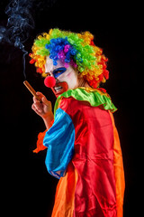 Evil clown on black background. Halloween mad woman is smoking cigar on black background. Portrait of crazy female with an angry look after performance.