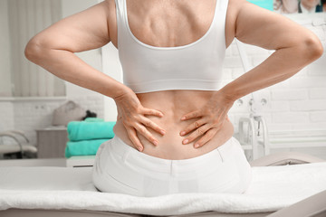 Elderly woman suffering from pain in back while sitting on massage table