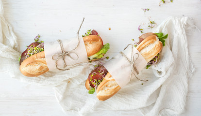 Sandwiches with beef, fresh vegetables and herbs over white wood backdrop, top view