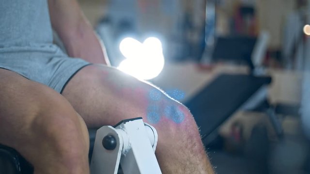 Young athlitic man does leg extensions in gym