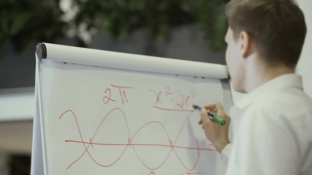 Young man writes formula on the flipchart
