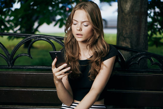girl sitting on a bench surrounded by trees and reading her smartphone