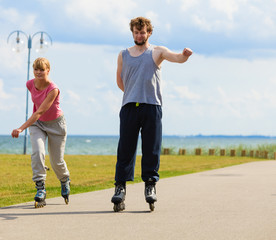 Obraz premium Young pair riding rollerblades in park.