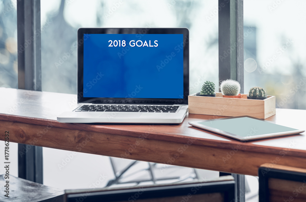 Poster Goals for 2018 word in laptop computer screen with tablet on wood stood table in at window with blur background,Digital Business or marketing trending.