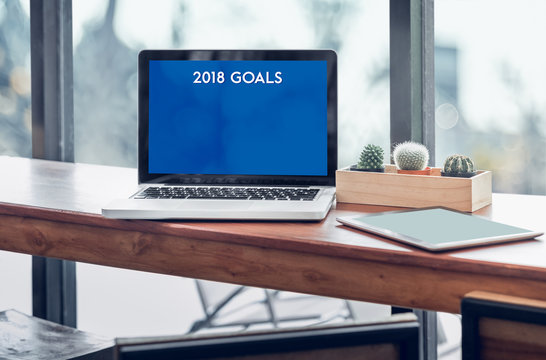 Goals for 2018 word in laptop computer screen with tablet on wood stood table in at window with blur background,Digital Business or marketing trending.