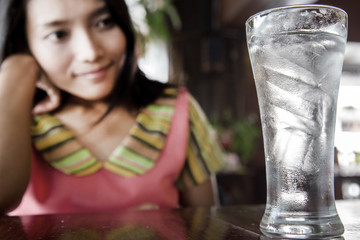 Asian girl sitting at a table with a glass of fresh water. The woman lokks on a full glass of water with ice.Drink water in the restaurant.