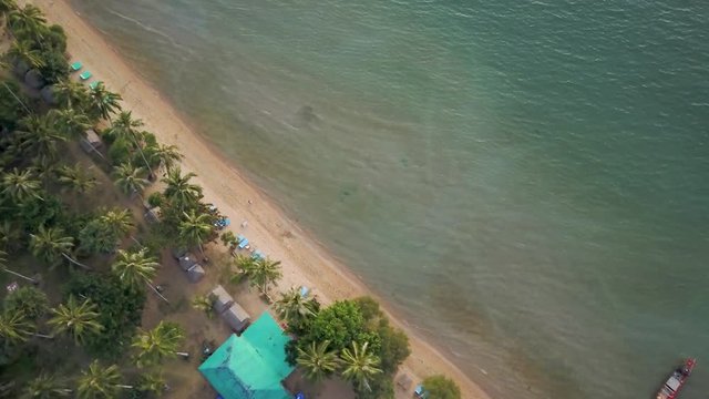 Looking straight down on paradise as aerial camera cuts diagonally across the beach to show palm trees at the shoreline with beach and boats in the aqua water.