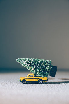 Christmas tree on yellow toy car over grey background.