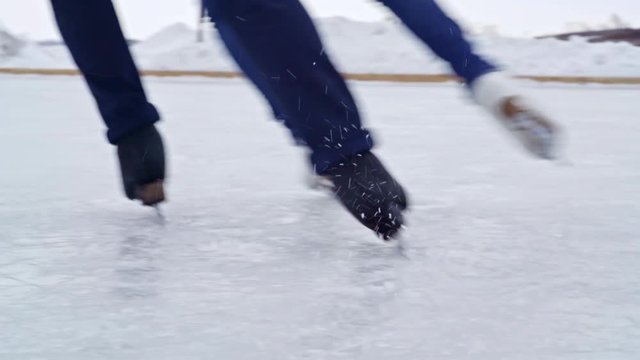 Tracking with low-section of legs of unrecognizable couple wearing jeans ice skating and practicing camel spin outdoors in winter