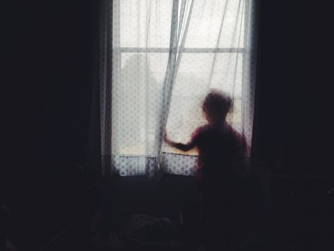 girl behind curtain looking out window