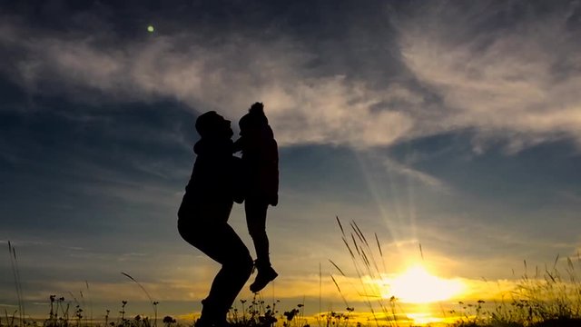 Father and little daughter silhouettes play at sunset. Father trowing happy child girl daughter air sunset landscape. Concept of friendly family. Slow Motion.