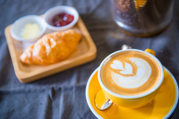 A cup of latte art with a croissant in cafe