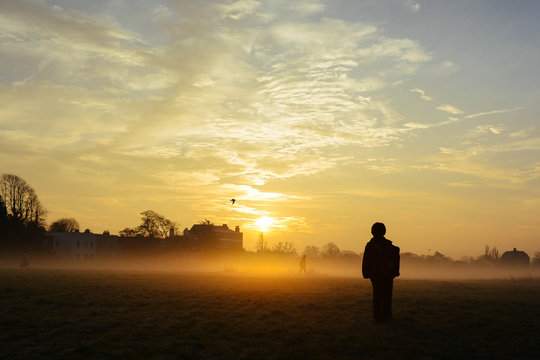 Rear view of boy standing outdoors during sunrise