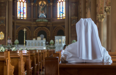 The nun sits in the church and prays to God. A nun in traditional white robes meditates in a...