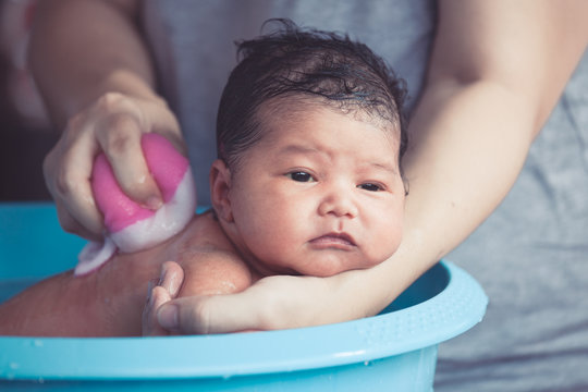 Cute Asian Newborn Baby Girl Take A Bath In Bathtub. Mom Cleaning Her Baby Body With Tenderness