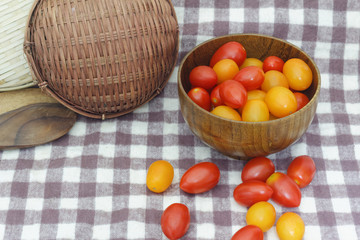 Small red cherry tomatoes spill out of a wicker basket on an old wooden table in rustic style, selective focus 