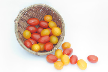 Small red and yellow cherry tomatoes spill out of a wicker basket on isolated white background